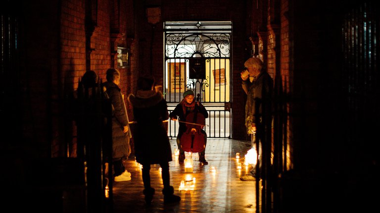Cellist performs for a small socially distanced group in a candle-lit alleyway