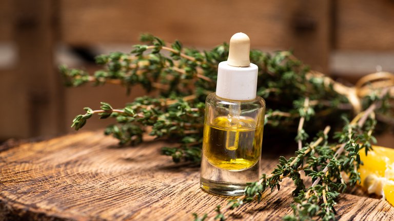Fresh herbs and essential oil in a glass vial sit on a rustic table